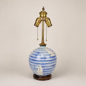 May include: A table lamp with a spherical ceramic base featuring horizontal blue and white stripes and white sailboat silhouettes. The lamp has a brass-colored metal neck, a double bulb socket, and two pull chains, all resting on a dark wooden base.