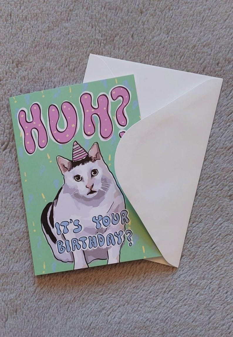 Op de afbeelding: Een groene verjaardagskaart met een witte kat die een roze feestmuts draagt. De kaart zegt "Huh? Is het je verjaardag?" in roze en blauwe letters.