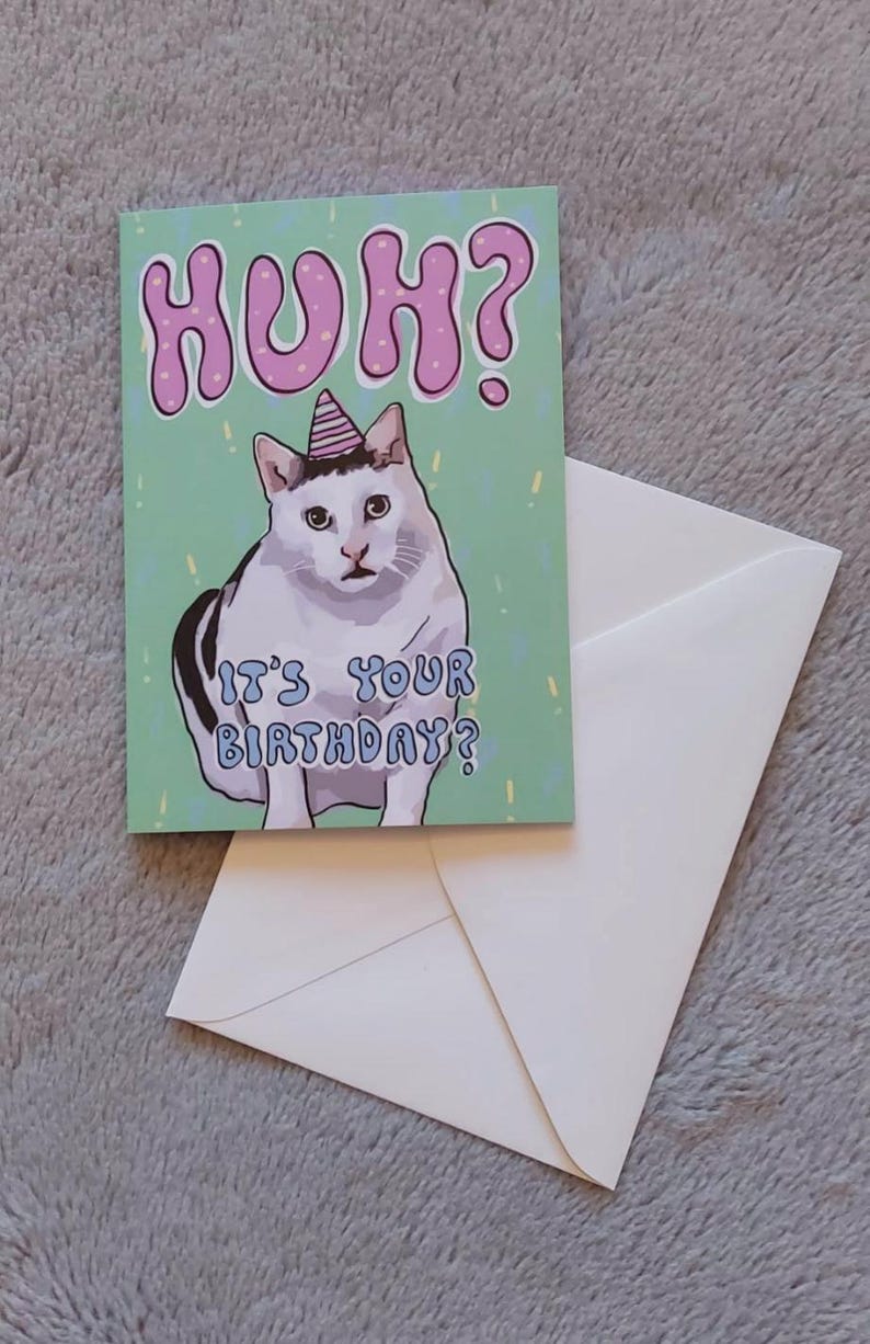 Op de afbeelding: Een groene verjaardagskaart met een witte kat die een roze feestmuts draagt. De kaart zegt "Huh? Is het je verjaardag?" in een kleurrijk lettertype.