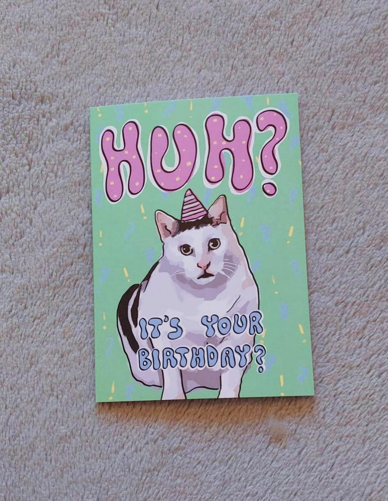 Op de afbeelding: Een verjaardagskaart met een witte kat die een roze feestmuts draagt. De kaart heeft een groene achtergrond met gele confetti en de tekst "HUH? Is het je verjaardag?" in roze en blauwe letters.