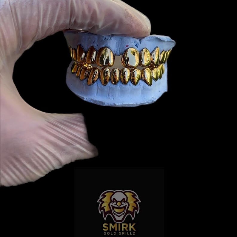 May include: A gold grillz set in a blue mold. The grillz are made of gold and have a diamond-shaped design. The mold is made of a soft, pliable material. The grillz are a popular accessory for hip-hop culture.