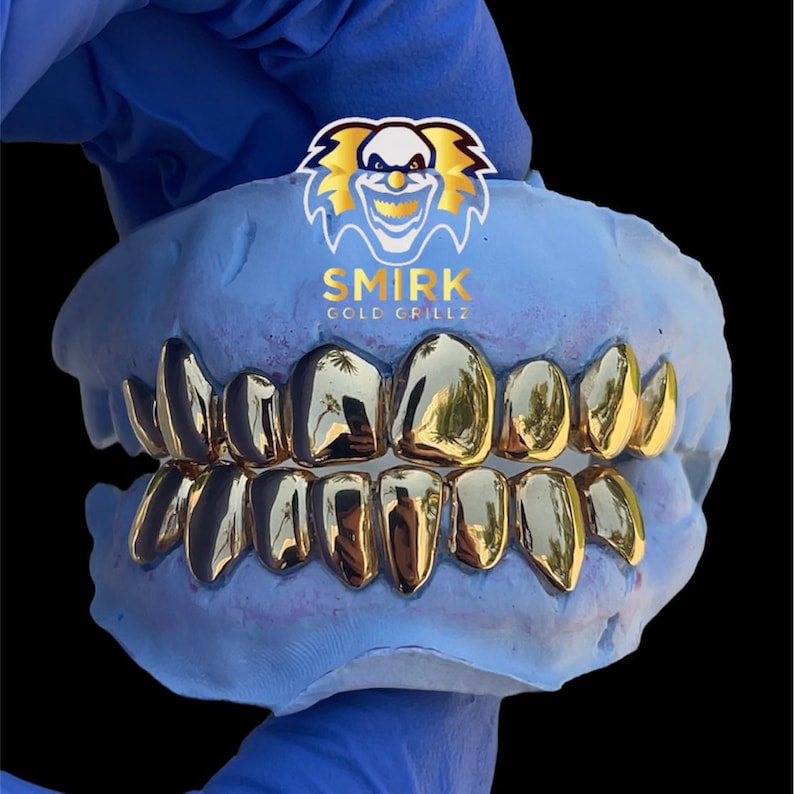 May include: Gold teeth grillz in a blue mold. The grillz are made of gold and have a shiny finish. The mold is made of a soft material and has a blue color. The grillz are in the shape of teeth and are designed to fit over the wearer's teeth. The grillz are a popular accessory for hip hop and rap artists.