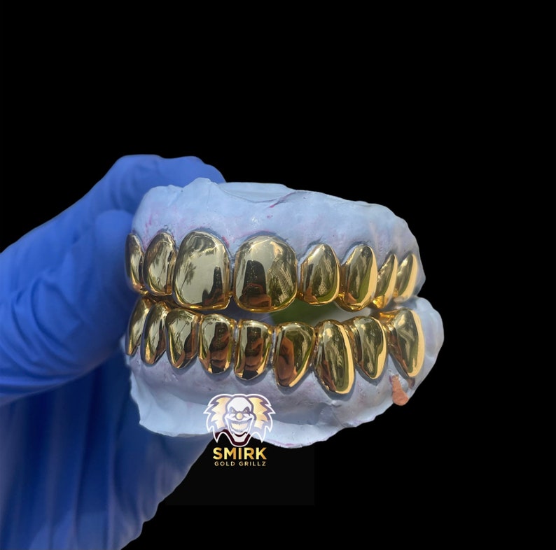 May include: Gold teeth grillz in a mold, with the brand name "Smirk Gold Grillz" printed below.