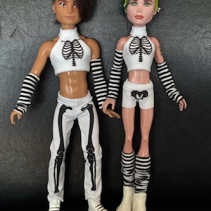 May include: Two fashion dolls in skeleton-themed outfits. They wear white crop tops with black ribcage designs, matching trousers or shorts, and striped arm warmers and socks. One doll has brown hair, the other green.