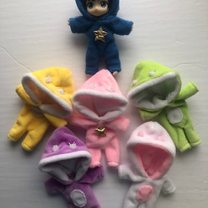 May include: Six plush hooded baby doll outfits in various colors, including yellow, pink, green, purple, and white. Each outfit has a star design and a white trim around the hood.