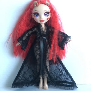 May include: A red-haired doll wearing a black lace robe with a black ribbon sash. The doll has blue eyes and red lipstick. The doll is wearing gold hair clips.