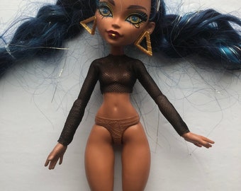 May include: A fashion doll with blue hair, brown skin, and gold jewelry. She is wearing a black mesh top and brown underwear.