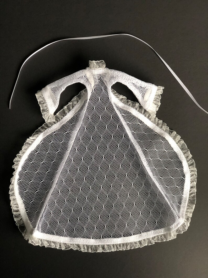 Pu&ograve; includere: Abito in tulle bianco con bordino in pizzo e un nastro da legare. L'abito &egrave; progettato per una bambola.