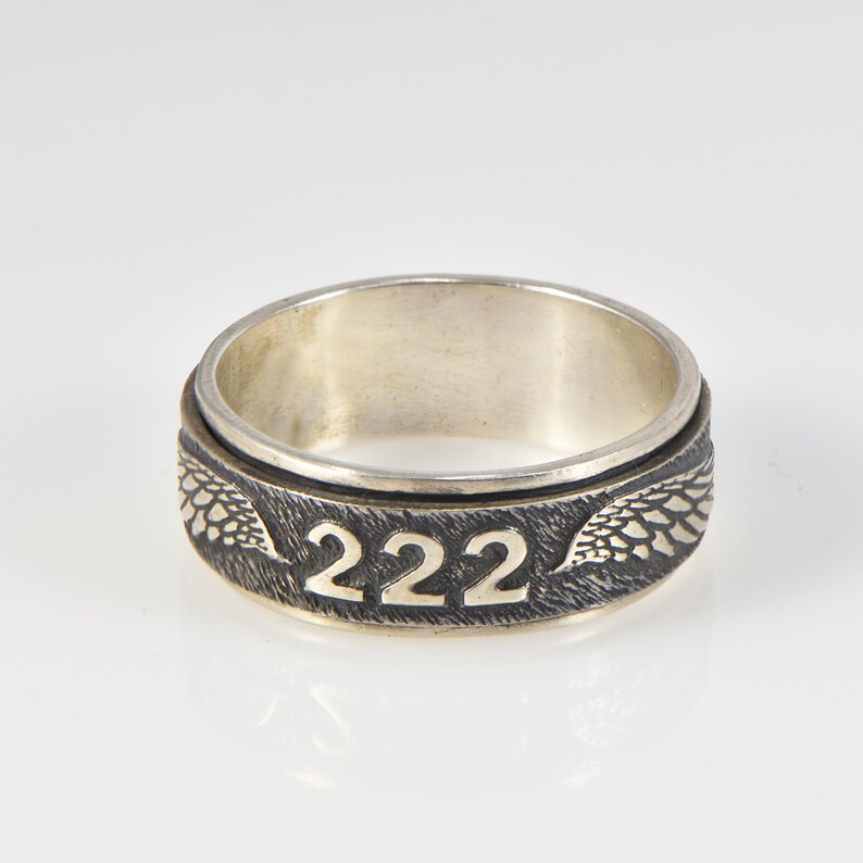May include: A silver spinning ring with the number 222 engraved on the band and a wing design on either side.