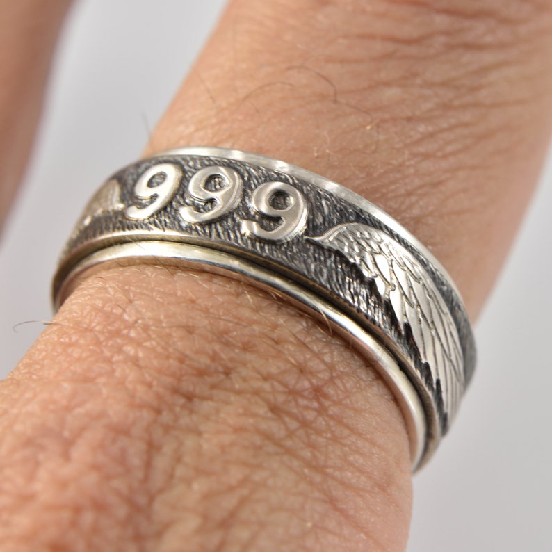 May include: A silver ring with the number 999 engraved on it. The ring also features a design of angel wings on the side.