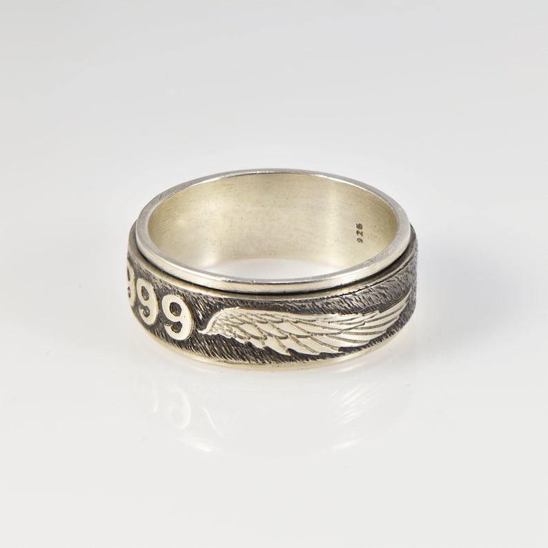 May include: A silver ring with a spinning band featuring the number 399 and a wing design. The ring is marked with "925" on the inside.