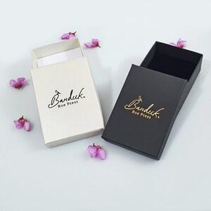 May include: Two small gift boxes with the logo "Banduk. Roe Press" printed on them. One box is white with black lettering and the other is black with gold lettering.