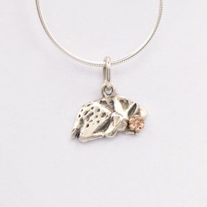 Può includere: Una collana in argento con un ciondolo a forma di cerbiatto a riposo con dettagli maculati. Il cerbiatto presenta un piccolo accento floreale color oro rosa vicino alla testa. Il ciondolo pende da una sottile catena d'argento rotonda e lucida.