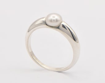 May include: A silver ring with a single, round, white pearl. The ring has a smooth, polished band that curves up to cradle the pearl. The pearl is centered on the ring, creating a simple and elegant design.