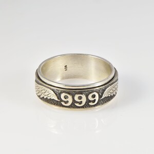 May include: A silver spinning ring with the number 999 engraved on the band and wings on either side. The ring is marked with 925.
