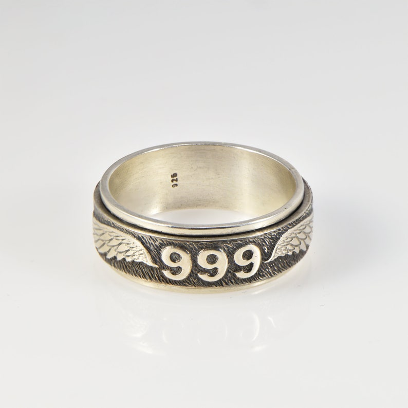 May include: A silver spinning ring with the number 999 engraved on the band and wings on either side. The ring is marked with 925.