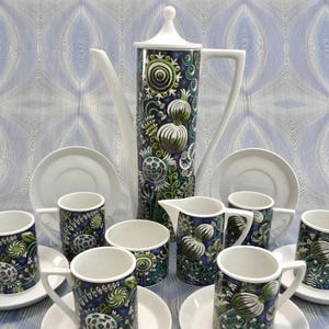 Puede incluir: Un juego de café vintage con una cafetera alta, tazas, platillos y una jarra de crema. El juego tiene una combinación de colores blanco y azul con un diseño botánico. La cafetera mide aproximadamente 30 cm de alto.