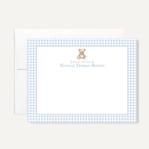May include: A personalized stationery set featuring a light blue gingham border. The stationery includes a teddy bear illustration and the text "from de nursery of Nicolas Thomas Morris" in a soft blue font. The set includes a white envelope.