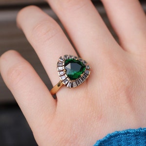 May include: A gold ring with a large, emerald green gemstone surrounded by smaller, clear gemstones.