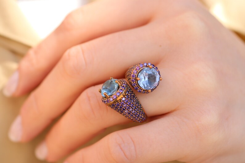 May include: A gold ring with two blue gemstones surrounded by purple stones.