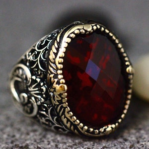 May include: A silver ring with an ornate design and a large, red gemstone.