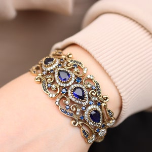 May include: A gold bracelet with intricate filigree designs and blue and clear gemstones.