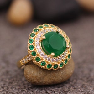 May include: A gold ring with a large green gemstone surrounded by smaller green and white stones.