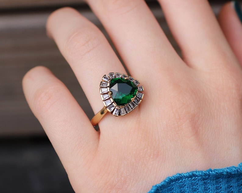May include: A gold ring with a large, emerald green gemstone surrounded by smaller, clear gemstones.