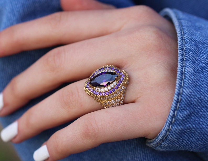 May include: A gold ring with a large, faceted, purple gemstone surrounded by smaller purple and white gemstones.