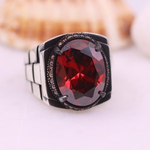 May include: A silver ring featuring a large, red, faceted gemstone set in a black bezel. The ring band has a textured, chain-like design.