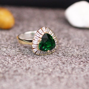 May include: A silver ring with a large green pear-shaped gemstone surrounded by smaller clear gemstones.