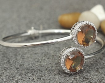 Puede incluir: Un brazalete de plata con dos piedras redondas marrones engastadas en un halo de piedras más pequeñas y transparentes.