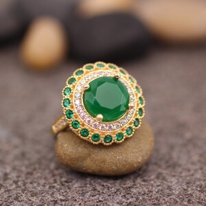 May include: A gold ring with a large green gemstone surrounded by smaller green and white gemstones.