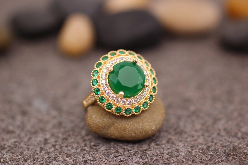 May include: A gold ring with a large green gemstone surrounded by smaller green and white gemstones.