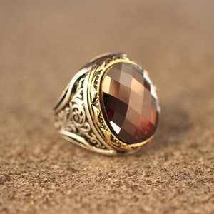 May include: A silver ring with an ornate design and a large, faceted, dark red gemstone.