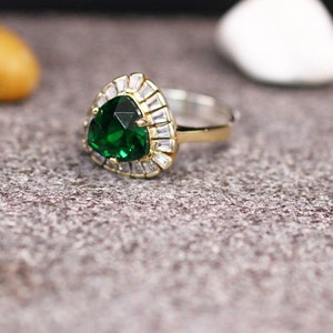 May include: A gold ring with a large, green, triangular gemstone surrounded by smaller, clear gemstones.