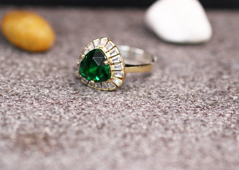 May include: A gold ring with a large, green, triangular gemstone surrounded by smaller, clear gemstones.