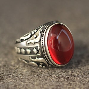 May include: A silver ring with an ornate design and a large, oval-shaped red gemstone.