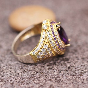 May include: A gold ring with a large purple gemstone surrounded by smaller white gemstones.