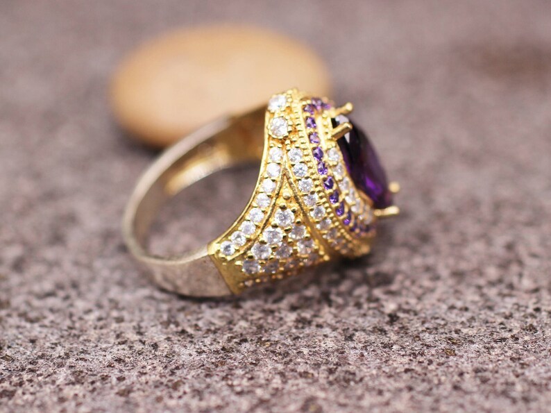 May include: A gold ring with a large purple gemstone surrounded by smaller white gemstones.