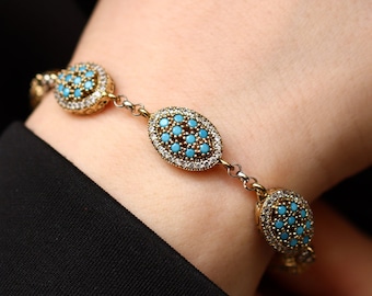 Può includere: Bracciale dorato con incastonature ovali e circolari di pietre color turchese, circondate da piccole pietre trasparenti. Il bracciale è collegato da piccole maglie argentate e viene indossato al polso.