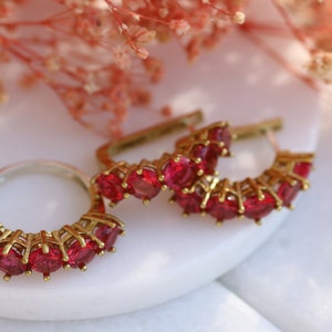 Peut inclure: Trois bagues en or serties de pierres rouges. Les bagues sont disposées en demi-cercle.