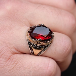 Peut inclure: Une bague en argent avec une grande pierre rouge de forme ovale sertie dans un entourage orné de couleur or.