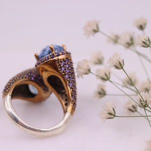 May include: A silver and gold ring with a large blue gemstone surrounded by smaller purple gemstones.