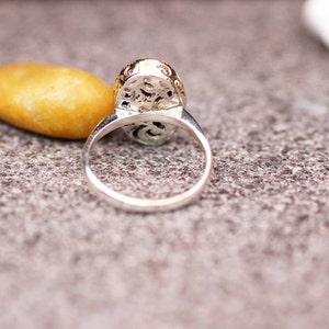 Pu&ograve; includere: Anello d'argento con castone ovale dettagliato con filigrana. L'anello &egrave; appoggiato su una superficie grigia strutturata, con una pietra gialla e una pietra bianca sullo sfondo. La fascia dell'anello &egrave; liscia e lucida.