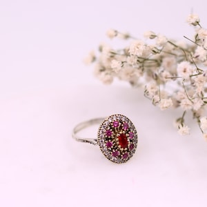 May include: A silver ring featuring a red and white oval-shaped stone surrounded by smaller stones.