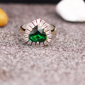 May include: A gold ring with a large, pear-shaped green gemstone surrounded by smaller clear gemstones.