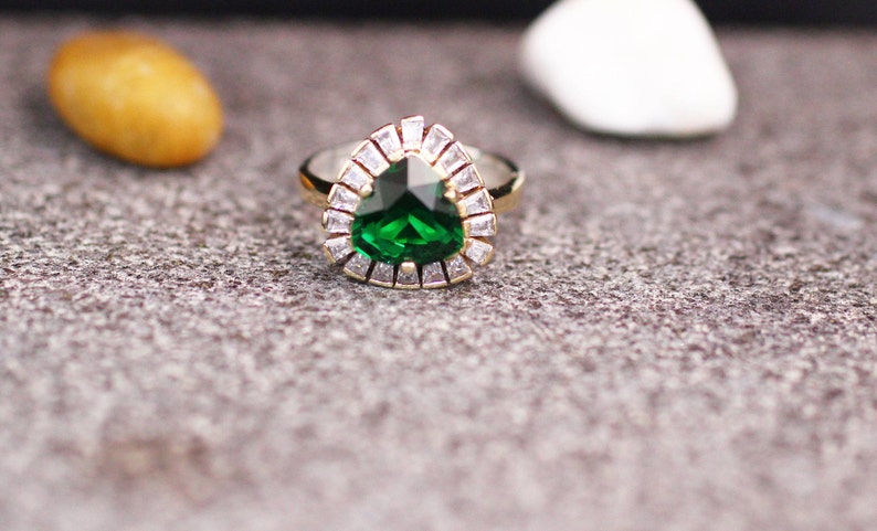 May include: A gold ring with a large, pear-shaped green gemstone surrounded by smaller clear gemstones.