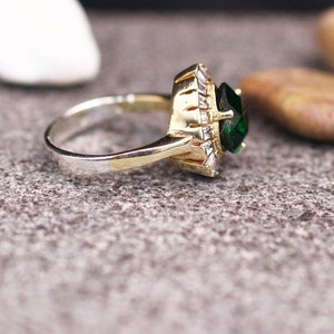 May include: A gold and silver ring with a large green gemstone surrounded by smaller clear gemstones.