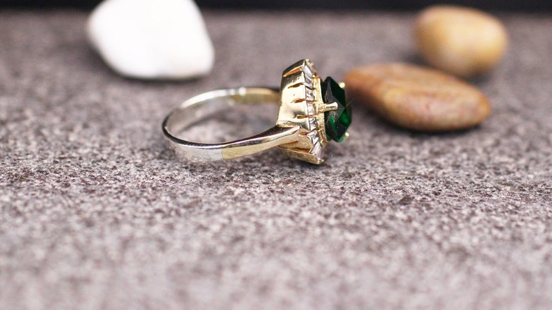 May include: A gold and silver ring with a large green gemstone surrounded by smaller clear gemstones.